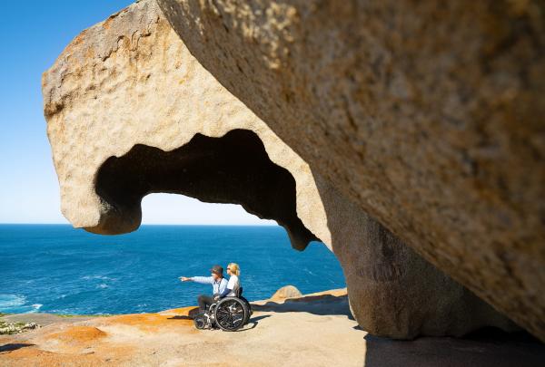Amidst the vibrant hues of Kangaroo Island's Remarkable Rocks, a person in a wheelchair and their enthusiastic tour guide share a moment of awe. Positioned against the brilliant, multicoloured rocks, they gaze out over the azure expanse of the Southern Ocean. The dynamic contrast between the vivid geological formations and the deep blue sea creates a visually stunning panorama, echoing the accessibility and inclusivity of the natural wonder they're enjoying © Tourism Australia
