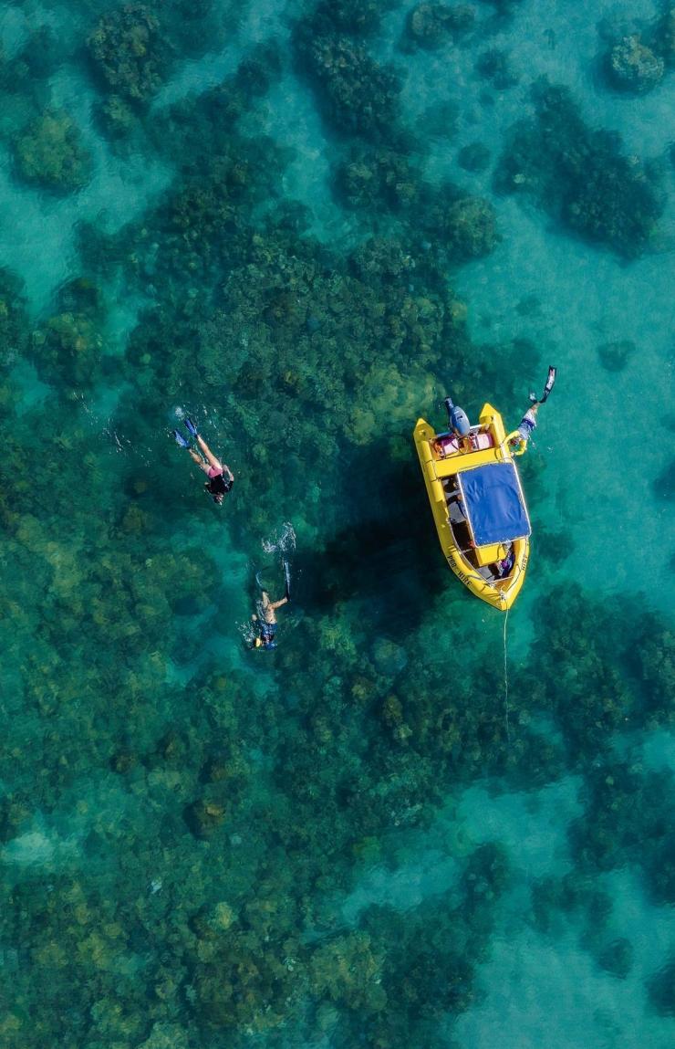 Aerial view of a group of people snorkelling next to a stationary yellow boat in the blue waters off Mackerel Islands in Exmouth, Western Australia © Tourism Australia