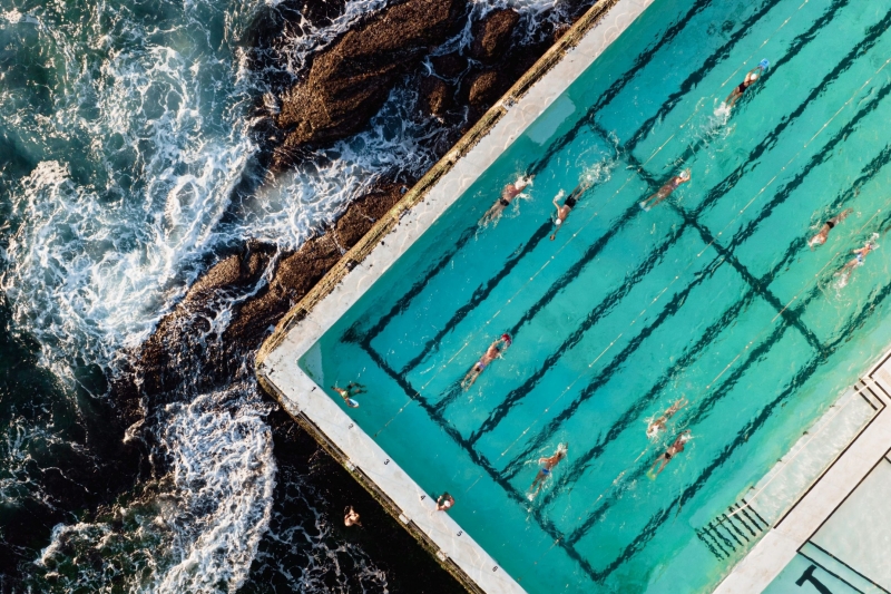 A captivating aerial view of swimmers enjoy Bondi Icebergs pool refreshing waters, while waves crash against its walls in Bondi, Sydney, New South Wales © Tourism Australia