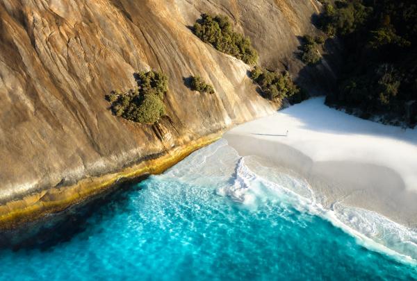 Aerial view of the clear blue waters and white sandy shore against the rock face of Misery Beach in Albany, Western Australia © @merewatson