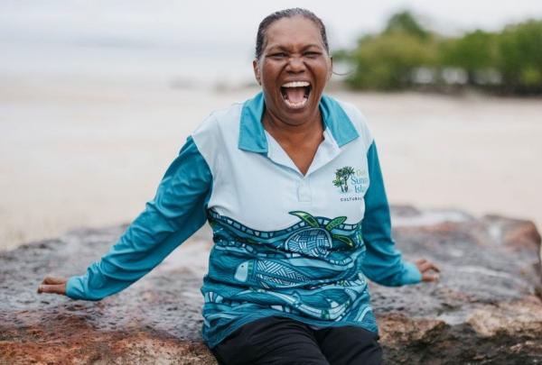 An  Oolin Sunday Cultural Tour sits joyfully on a rock against a coastal backdrop.