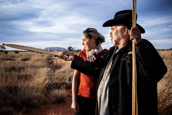 A guide and tour attendee explore the outback of Uluṟu-Kata Tjuṯa National Park, with Uluṟun in the background.  © Tourism Australia