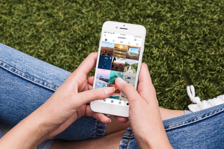 Person sitting down with their mobile phone looking at Tourism Australia's Instagram account © Tourism Australia