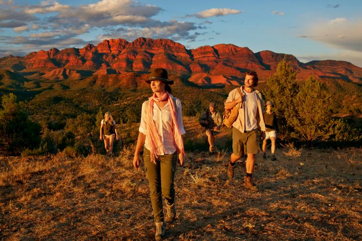 A group of people walk through the wilderness with a red mountain range in the background. A group of people walk through the wilderness with a red mountain range in the background.